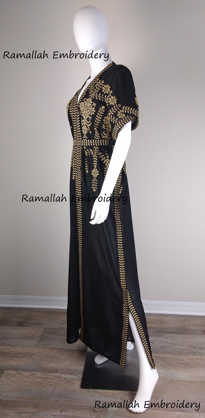 May include: Black maxi dress with gold embroidery. The dress features a V-neck, short sleeves, and a slit on the side. The dress is displayed on a mannequin. The text "Ramallah Embroidery" is visible.
