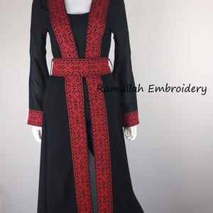 Puede incluir: Una larga abaya negra con bordados rojos. La abaya tiene un escote en V y un cintur&oacute;n. El bordado es intrincado y detallado. La abaya es una prenda tradicional que usan las mujeres en muchas culturas.