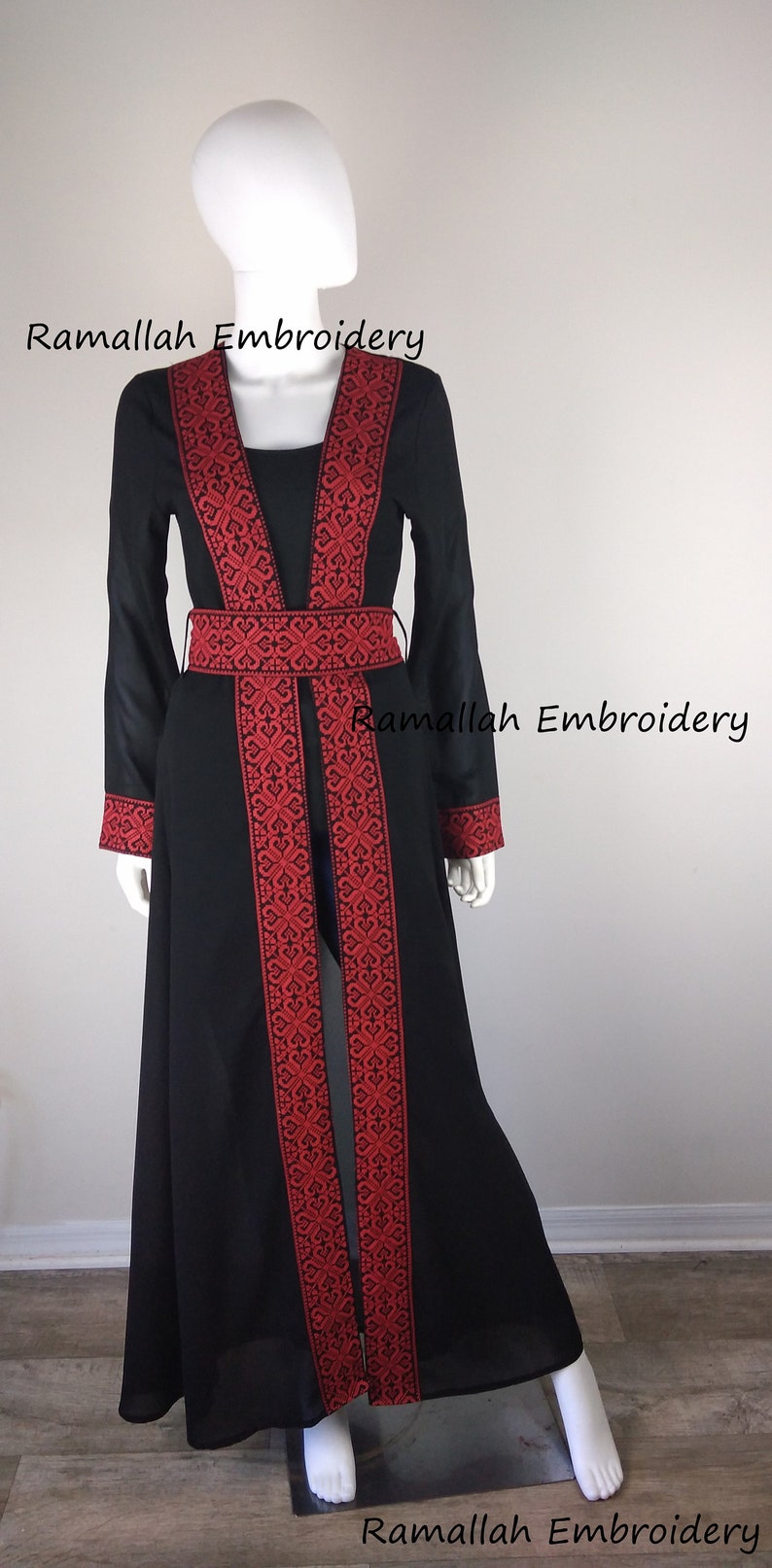 Puede incluir: Una larga abaya negra con bordados rojos. La abaya tiene un escote en V y un cintur&oacute;n. El bordado es intrincado y detallado. La abaya es una prenda tradicional que usan las mujeres en muchas culturas.