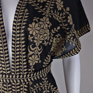 May include: Black garment with intricate gold embroidery, featuring floral and geometric patterns. The text "Ramallah Embroidery" is visible. The design includes a detailed border and floral motifs, showcasing traditional craftsmanship.
