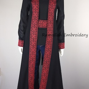 Puede incluir: Una larga chaqueta negra con ribetes bordados en rojo. La chaqueta tiene una silueta larga y fluida y es perfecta para superponer sobre un vestido o pantalones.