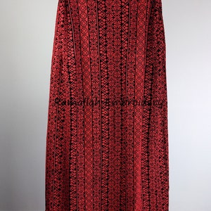 May include: A red and black embroidered cape with a geometric pattern. The cape is on a white mannequin. The text "Ramallah Embroidery" is visible at the top and bottom of the image.