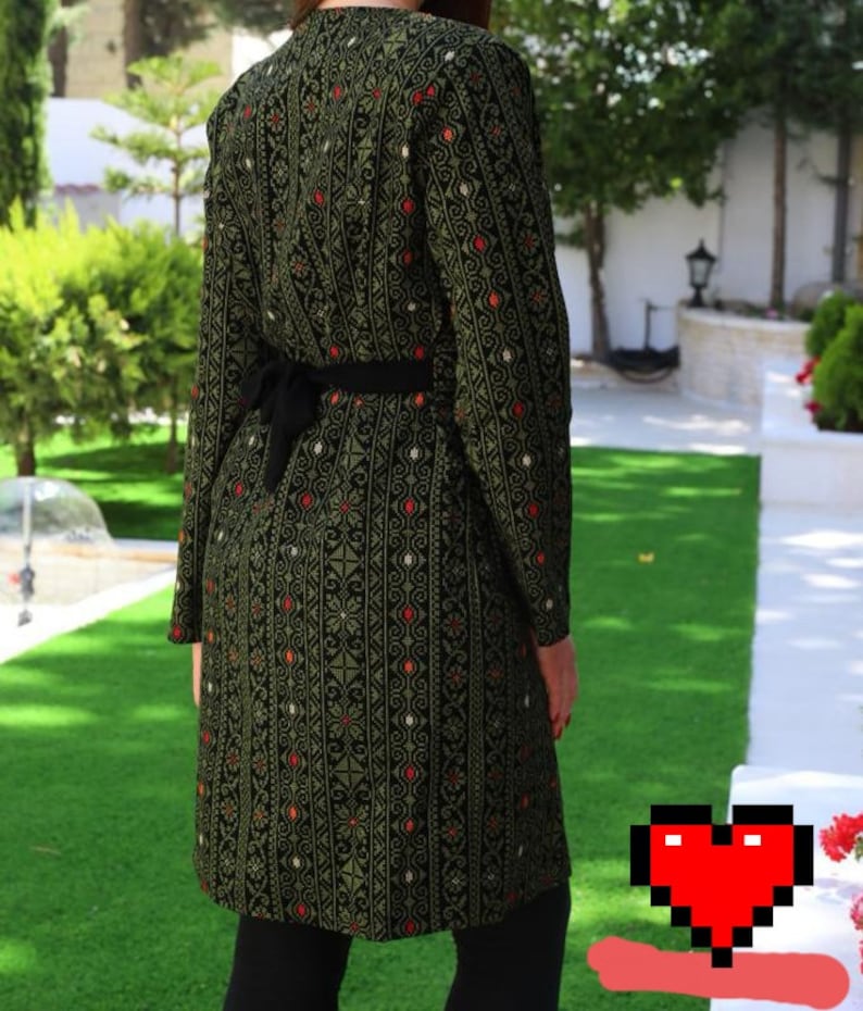 May include: A long, green and black patterned dress with a black belt. The dress has a traditional embroidered design with red and white accents.