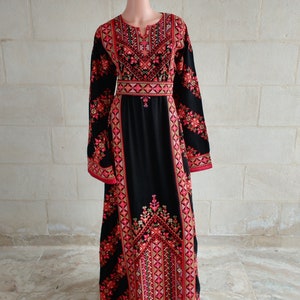 May include: A long black dress with intricate red and gold embroidery. The dress has a high neckline and long sleeves. The embroidery features geometric patterns and floral motifs.