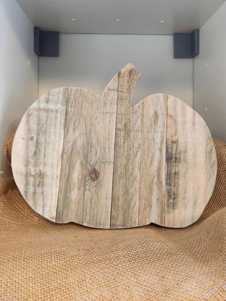 Puede incluir: Una decoraci&oacute;n de calabaza r&uacute;stica de madera. La calabaza est&aacute; hecha de tablas de madera de color claro, ensambladas para formar la forma de la calabaza. Tiene un tallo y est&aacute; sobre una superficie de arpillera. La madera tiene variaciones naturales de color.