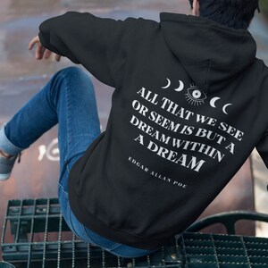 May include: Black hooded sweatshirt with a white print that reads "All that we see or seem is but a dream within a dream" and "Edgar Allan Poe" on the back. The print also includes a stylized eye and crescent moons.
