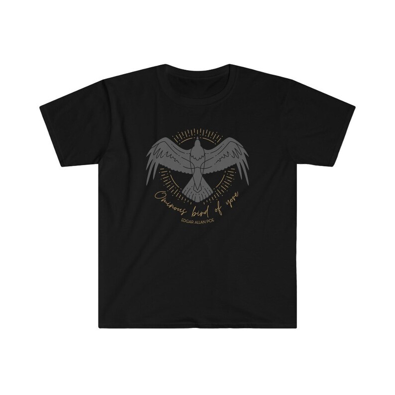 Puede incluir: Camiseta negra con un gr&aacute;fico de un cuervo en vuelo, rodeado de un c&iacute;rculo de rayos de sol. El texto "Once upon a midnight dreary" y "Edgar Allan Poe" est&aacute;n impresos debajo del cuervo.