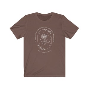 May include: A brown t-shirt with a white graphic design featuring a hand holding a flower with the text "It is not in the stars to hold our destiny but in ourselves" and "William Shakespeare".