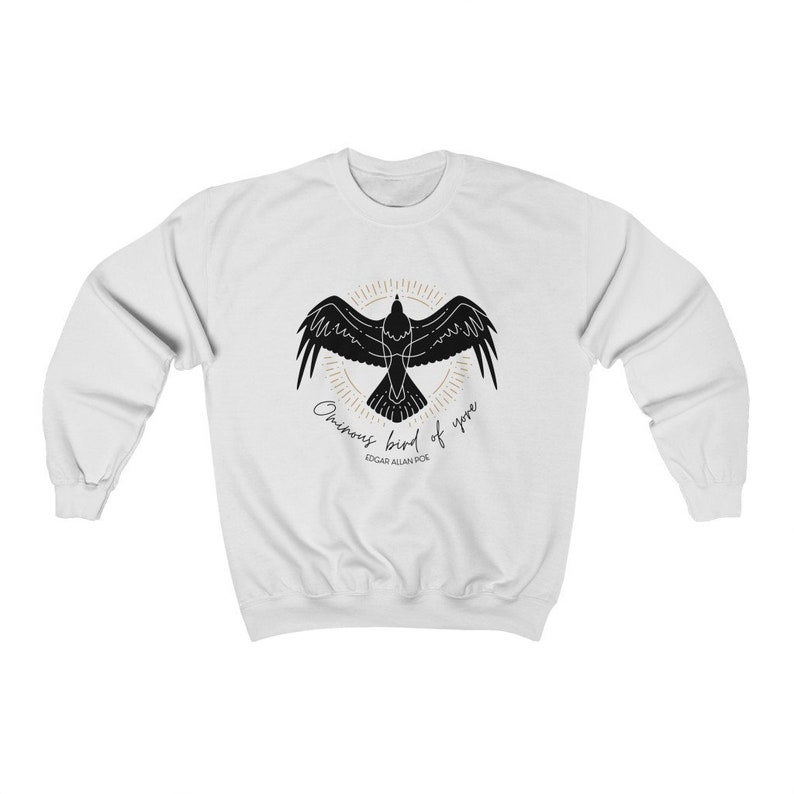 K&ouml;nnte beinhalten: Wei&szlig;er Pullover mit einer schwarzen Silhouette eines Rabens mit dem Text "Once upon a midnight dreary" und "Edgar Allan Poe" auf der Vorderseite.