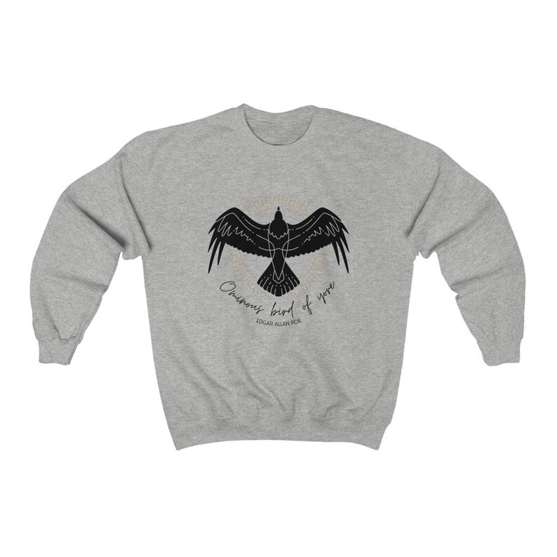 K&ouml;nnte beinhalten: Ein graues Sweatshirt mit einer schwarzen Silhouette eines Rabens im Flug und dem Text "Ominous bird of yore" und "Edgar Allan Poe" darunter.