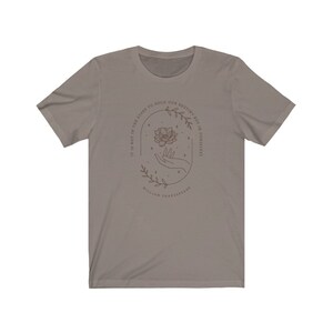 May include: A gray t-shirt with a brown outline of a hand holding a flower with stars around it. The text reads "It is not in the stars to hold our destiny but in ourselves" and "William Shakespeare".