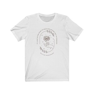 May include: White t-shirt with a floral design and the quote "It is not in the stars to hold our destiny but in ourselves" by William Shakespeare.