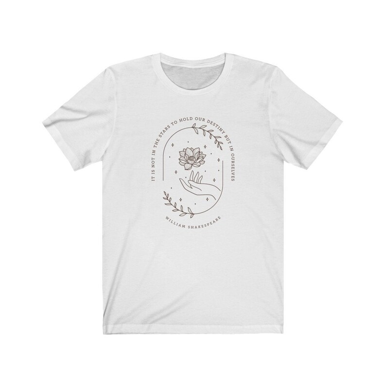 May include: White t-shirt with a floral design and the quote "It is not in the stars to hold our destiny but in ourselves" by William Shakespeare.