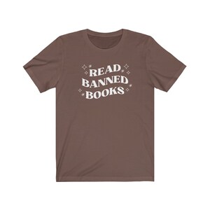 May include: A brown t-shirt with the text "READ BANNED BOOKS" in white lettering with stars around the text.