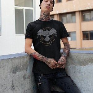 Puede incluir: Una camiseta negra con un gr&aacute;fico de un p&aacute;jaro en vuelo con el texto "Ominous bird of you" y "Edgar Allan Poe" debajo. La persona que lleva la camiseta tiene tatuajes en los brazos y el cuello.