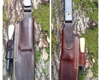 Może przedstawiać: Dwie skórzane pochwy na noże w kolorze ciemnobrązowym z ozdobnymi przeszyciami. Każda pochwa ma pętlę na pasek i małą kieszeń na nóż i krzesiwo.