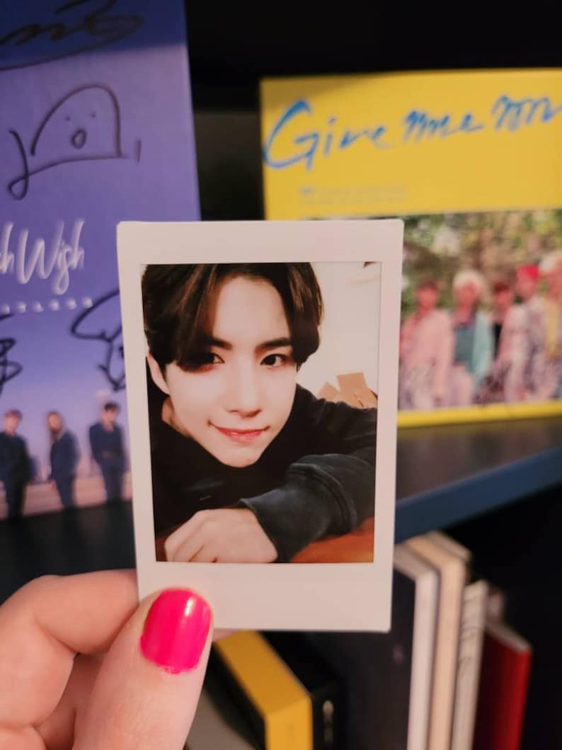 May include: A Polaroid photo of a young man with dark hair. He is wearing a black sweater and looking at the camera. The photo is held in a hand with pink nail polish.