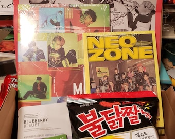 Könnte beinhalten: Eine Schachtel gefüllt mit verschiedenen K-Pop-Artikeln, darunter Alben, Foto-Karten und Snacks. Die Alben zeigen die Gruppen NCT, Ateez und Stray Kids. Die Foto-Karten zeigen Mitglieder der Gruppen NCT und Stray Kids. Die Snacks sind eine Tüte scharfe koreanische Ramen-Nudeln.