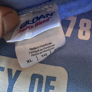 Peut inclure: Un t-shirt bleu clair Gildan Heavy Blend avec du texte blanc qui dit "Y OF 78". L'&eacute;tiquette indique "Fabriqu&eacute; au Honduras, Made in Honduras, Hecho en Honduras" et la taille est XL.