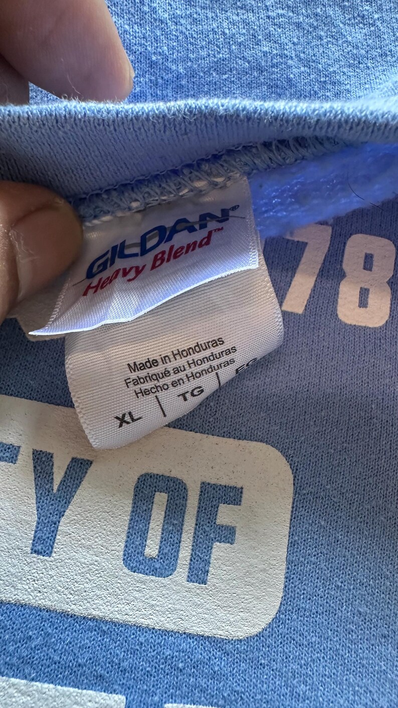 Peut inclure: Un t-shirt bleu clair Gildan Heavy Blend avec du texte blanc qui dit "Y OF 78". L'&eacute;tiquette indique "Fabriqu&eacute; au Honduras, Made in Honduras, Hecho en Honduras" et la taille est XL.
