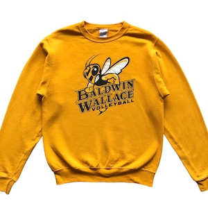 May include: Mustard yellow sweatshirt with a bee graphic and the text "BALDWIN WALLACE VOLLEYBALL". The design is in black and gold. The sweatshirt has a crew neck and long sleeves. A casual top.