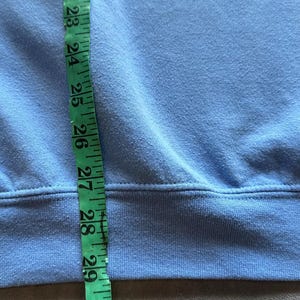 Peut inclure: Un sweat-shirt bleu clair avec un ourlet c&ocirc;tel&eacute;. Un m&egrave;tre ruban est plac&eacute; le long du c&ocirc;t&eacute; du sweat-shirt, montrant une longueur de 71 cm.