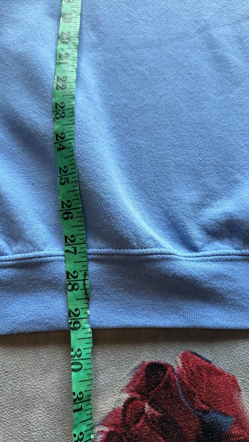 Peut inclure: Un sweat-shirt bleu clair avec un ourlet c&ocirc;tel&eacute;. Un m&egrave;tre ruban est plac&eacute; le long du c&ocirc;t&eacute; du sweat-shirt, montrant une longueur de 71 cm.