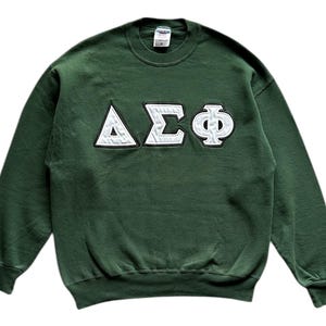 May include: A dark green sweatshirt with white Greek letters ΔΣΦ. The letters are stitched onto the front of the sweatshirt. The sweatshirt has a crew neck and ribbed cuffs and hem.