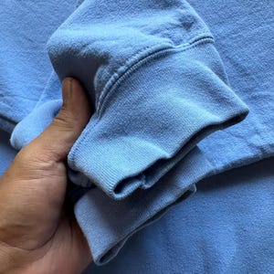 Peut inclure: Un gros plan sur le poignet pli&eacute; d'un sweat-shirt bleu clair. Le tissu est doux et textur&eacute;.