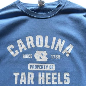 Peut inclure: Un sweat-shirt bleu clair avec du texte blanc qui dit "Carolina since 1789 Property of Tar Heels".