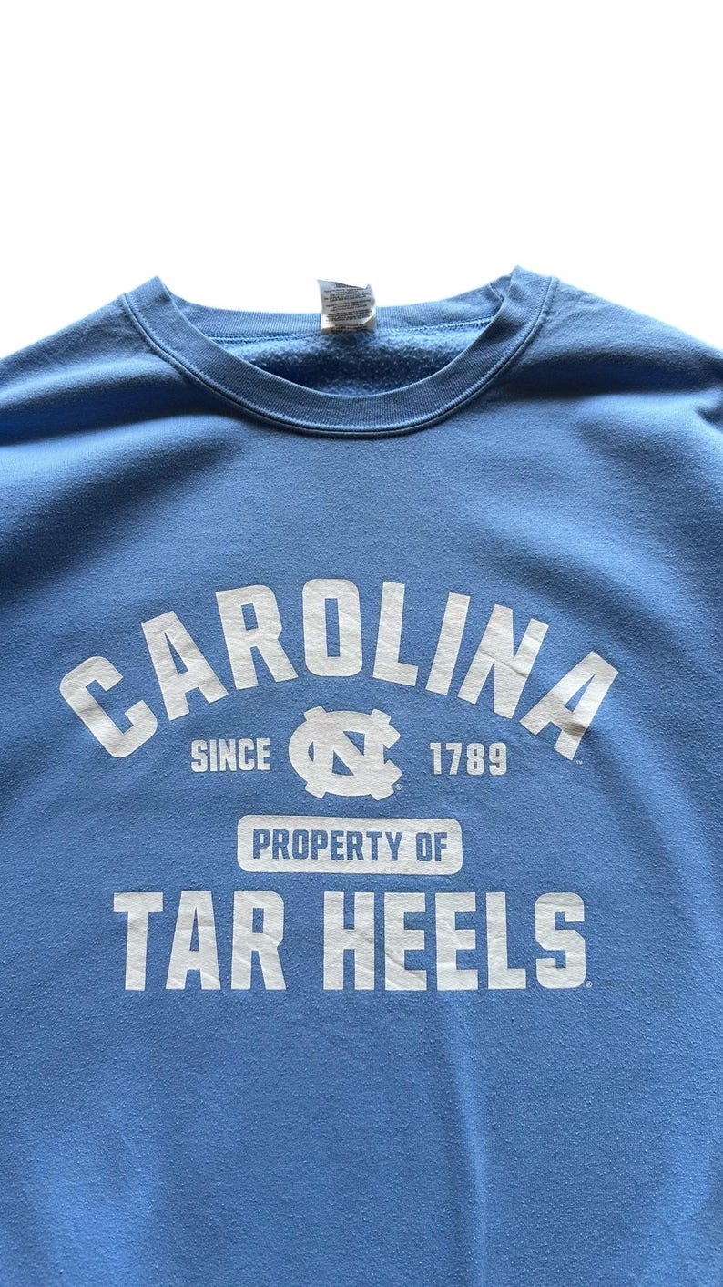 Peut inclure: Un sweat-shirt bleu clair avec du texte blanc qui dit "Carolina since 1789 Property of Tar Heels".