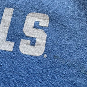 Peut inclure: Gros plan sur un tissu bleu clair avec le mot "S" en lettres blanches. Le tissu a une surface textur&eacute;e.
