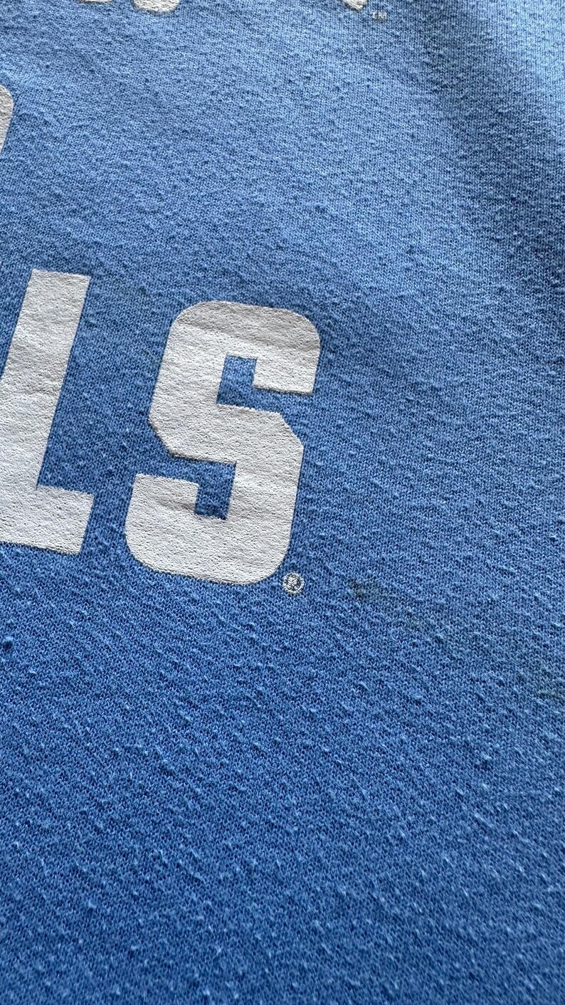 Peut inclure: Gros plan sur un tissu bleu clair avec le mot "S" en lettres blanches. Le tissu a une surface textur&eacute;e.
