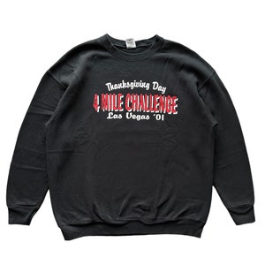 Puede incluir: Sudadera negra con un estampado gráfico blanco que dice "Thanksgiving Day 4 Mile Challenge Las Vegas '01"