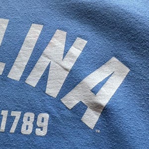 Peut inclure: Un t-shirt bleu avec un lettrage blanc qui dit "INA 1789" avec un symbole de marque d&eacute;pos&eacute;e.