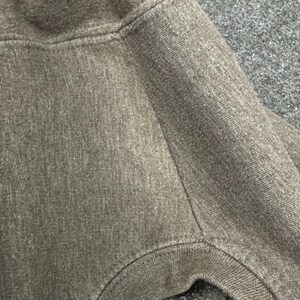 May include: Close-up of a grey hooded sweatshirt. The fabric is a soft, textured knit with visible stitching along the seams. The hood and shoulder area are in focus, showing the garment's construction.