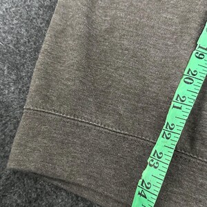 May include: Close-up of dark grey fabric with a sewn hem. A green measuring tape is laid across the fabric, showing measurements from 48 to 69 cm.