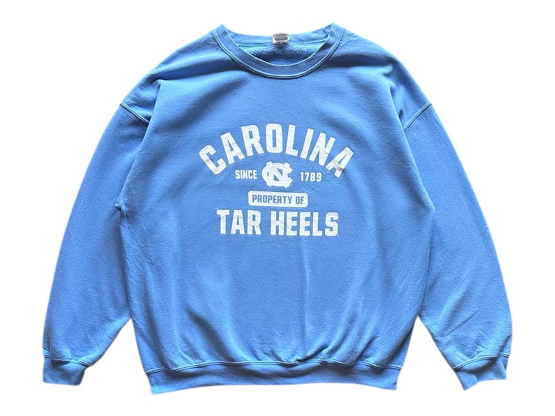 Peut inclure: Un sweat-shirt bleu clair avec le texte "CAROLINA SINCE 1789 PROPERTY OF TAR HEELS" en blanc.