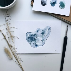 Könnte beinhalten: Ein Aquarellbild einer blauen und grünen abstrakten Form auf weißem Hintergrund. Das Bild ist unten rechts mit "LMT" signiert.