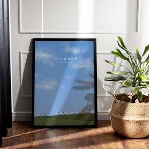 Könnte beinhalten: Ein schwarzer gerahmter Druck mit blauem Himmel und weißen Wolken. Der Druck zeigt "PELLWORM 54° 30' 17" N 8° 30' 12" O" und eine Reihe weißer Schafe, die über ein grünes Feld laufen.