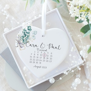 May include: White ceramic heart ornament with a floral design and the text "Cara & Paul Married August 2023" with the wedding date circled in red.