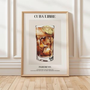 Puede incluir: Una impresión enmarcada con una ilustración del cóctel Cuba Libre. La bebida está en un vaso alto con cubitos de hielo y una rodaja de lima. El texto "CUBA LIBRE" está en la parte superior, con "INGREDIENTS" y la receta debajo. El marco es de color madera clara.