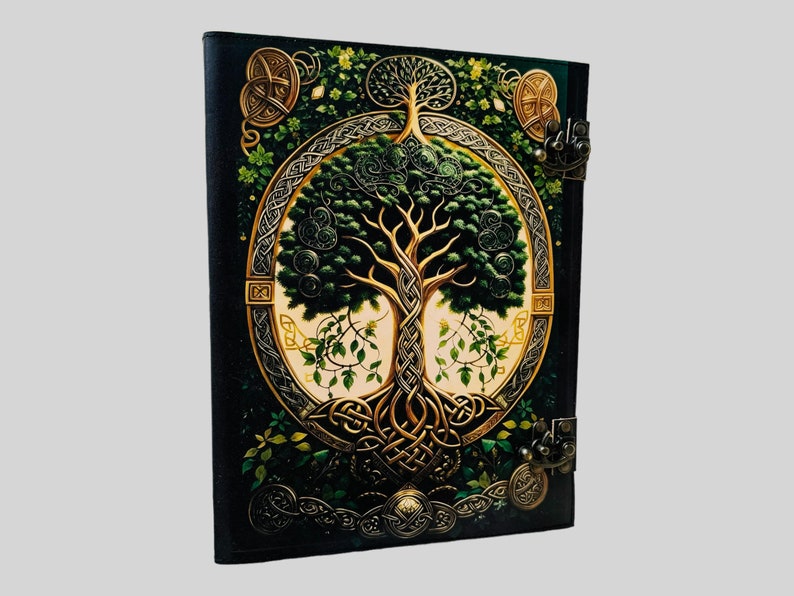 May include: A black leather journal with a gold Celtic knot design and a green tree of life illustration. The journal has two metal clasps.
