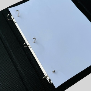 May include: A black three-ring binder with a white page inserted. The binder has silver rings.