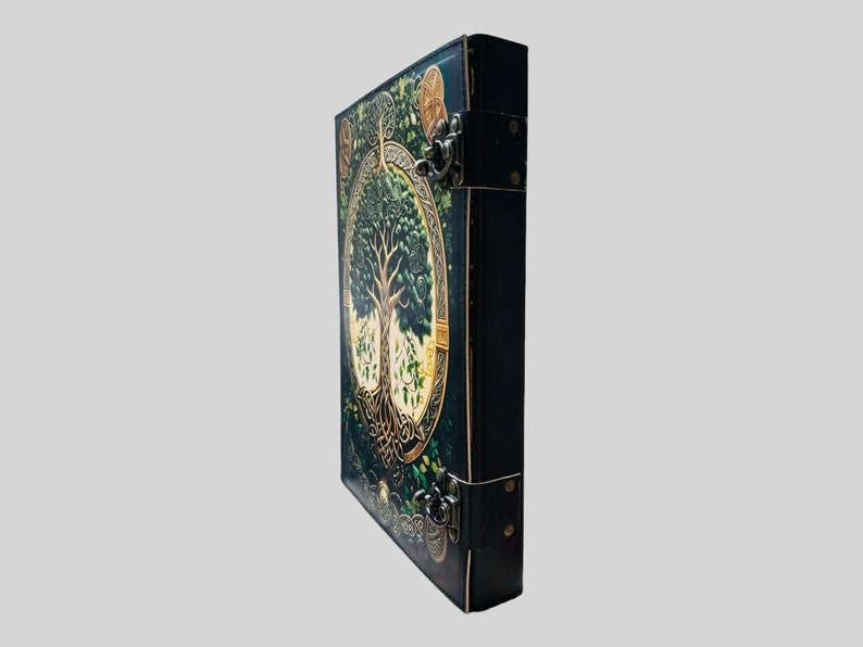 May include: A black leather-bound journal with a detailed illustration of a tree of life on the front cover. The cover features gold accents and intricate details. The journal has two metal clasps.