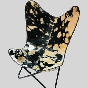 Op de afbeelding: Een zwart-witte butterfly stoel van koeienhuid met een zwart metalen frame.