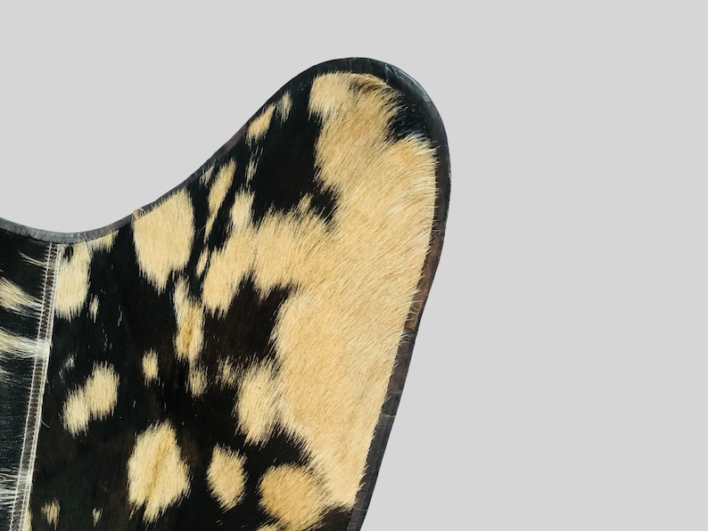 Op de afbeelding: Close-up van de rugleuning van een stoel van zwart en bruin koeienhuid. De stoel heeft een gebogen rugleuning en een zwarte leren rand.