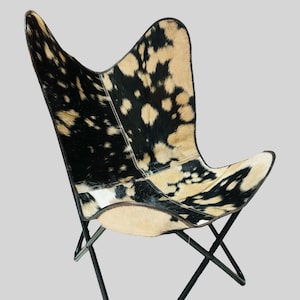 Op de afbeelding: Een zwart-witte butterfly stoel van koeienhuid met een zwart metalen frame. De stoel is gemaakt van echt koeienhuid en heeft een uniek, natuurlijk patroon.