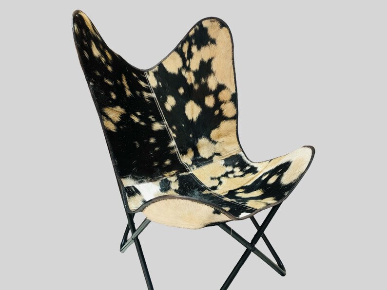 Op de afbeelding: Een zwart-witte butterfly stoel van koeienhuid met een zwart metalen frame. De stoel is gemaakt van echt koeienhuid en heeft een uniek, natuurlijk patroon.