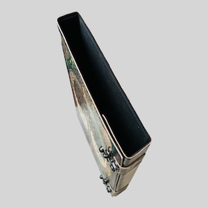 May include: A brown leather journal with a colorful, intricate design on the front cover. The journal has a black fabric lining and metal accents.